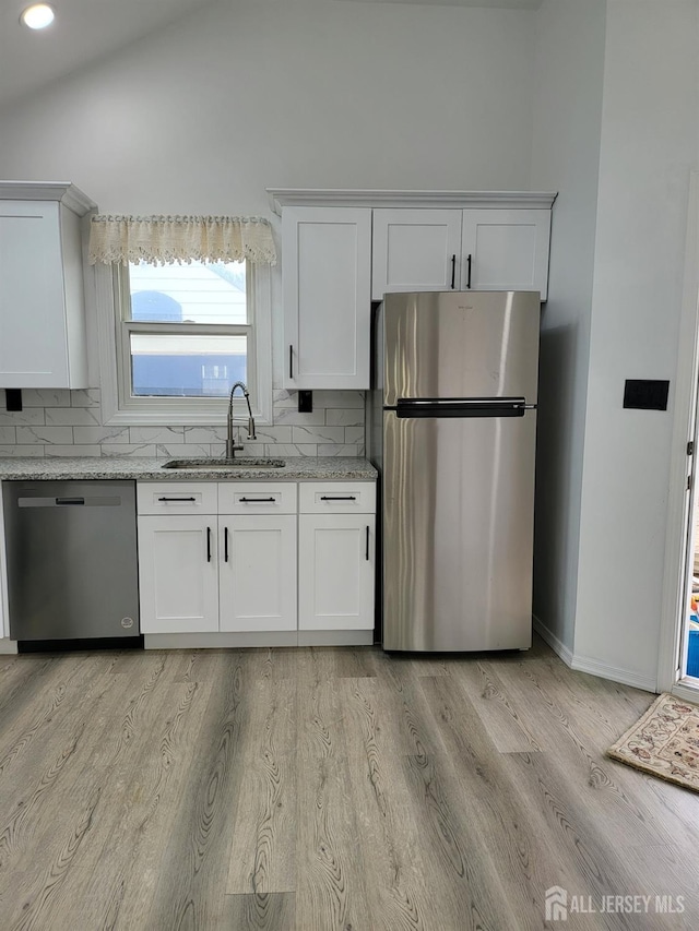 kitchen with light wood finished floors, light stone countertops, appliances with stainless steel finishes, white cabinets, and a sink