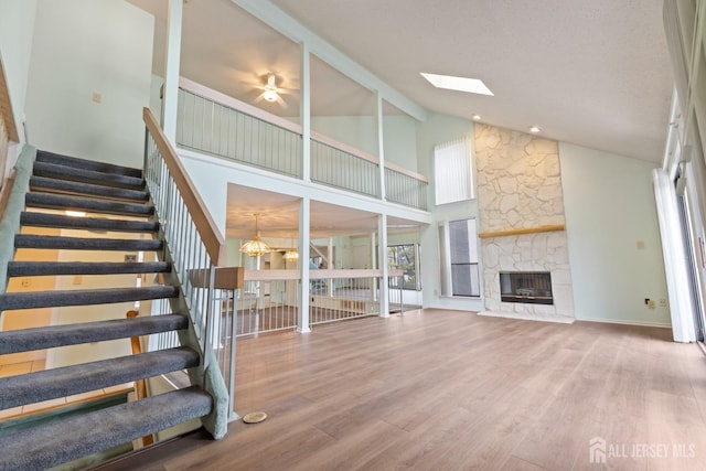 unfurnished living room featuring an inviting chandelier, a fireplace, hardwood / wood-style floors, and lofted ceiling with skylight