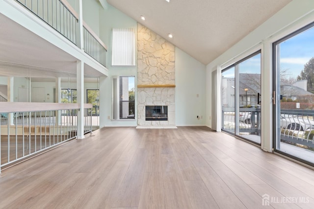 unfurnished living room featuring a stone fireplace, light hardwood / wood-style flooring, high vaulted ceiling, and plenty of natural light