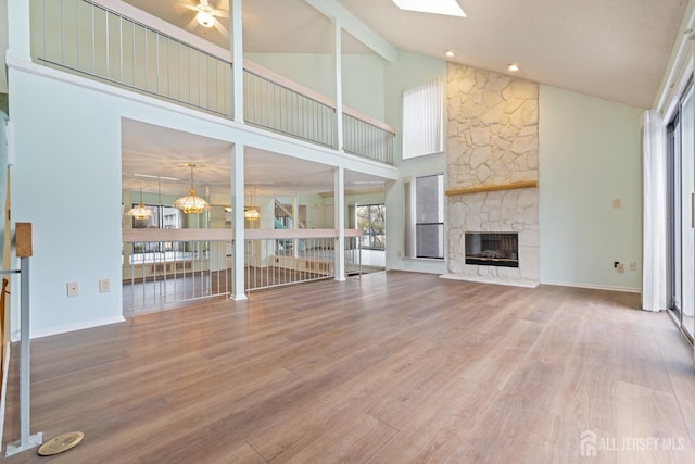 unfurnished living room with hardwood / wood-style flooring, ceiling fan, a stone fireplace, and a skylight