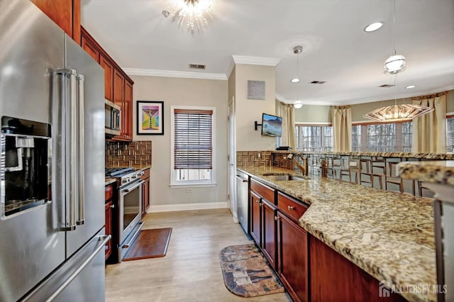 kitchen featuring stainless steel appliances, a sink, visible vents, hanging light fixtures, and light stone countertops