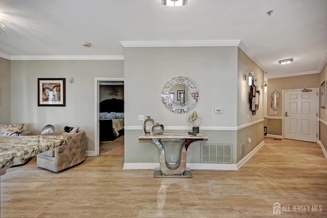 foyer entrance featuring light wood finished floors, baseboards, visible vents, and crown molding