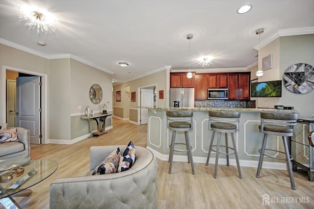 kitchen featuring light stone counters, stainless steel appliances, light wood-style floors, hanging light fixtures, and decorative backsplash