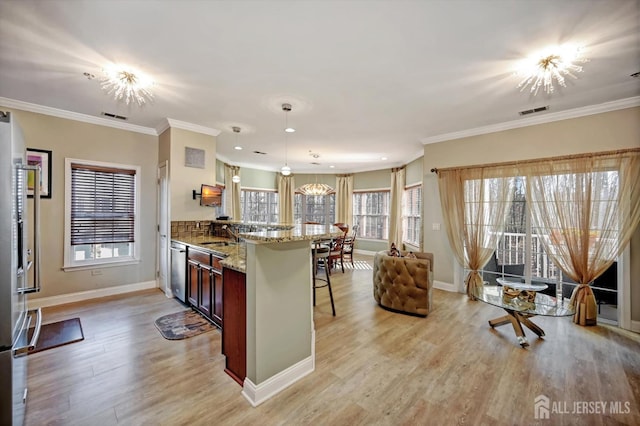 kitchen with a notable chandelier, stainless steel appliances, visible vents, a kitchen breakfast bar, and decorative light fixtures