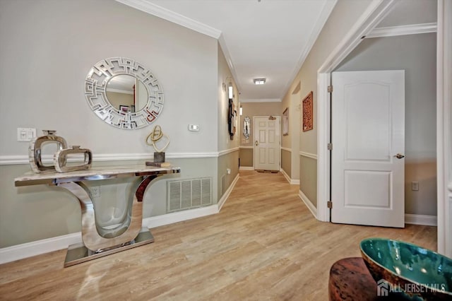 hallway featuring light wood-type flooring, visible vents, crown molding, and baseboards