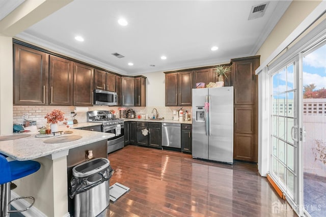 kitchen with light stone counters, dark hardwood / wood-style flooring, decorative backsplash, a breakfast bar, and appliances with stainless steel finishes