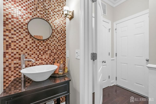 bathroom featuring hardwood / wood-style flooring, vanity, crown molding, and tasteful backsplash