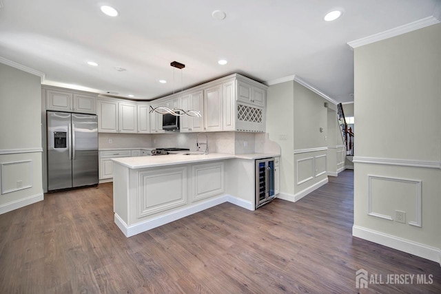 kitchen with appliances with stainless steel finishes, beverage cooler, crown molding, light countertops, and a peninsula