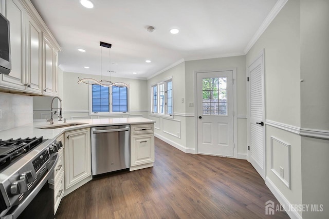 kitchen with appliances with stainless steel finishes, a sink, a peninsula, a wainscoted wall, and crown molding
