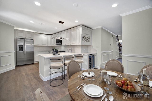 kitchen with stainless steel appliances, wine cooler, light countertops, a decorative wall, and a peninsula