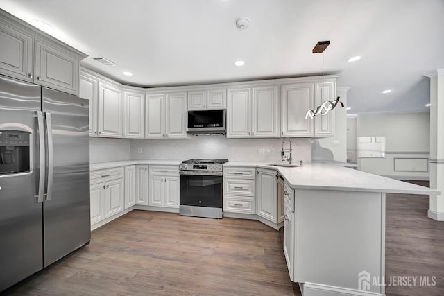 kitchen featuring stainless steel appliances, a peninsula, a sink, light countertops, and wood finished floors