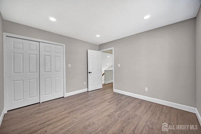 unfurnished bedroom featuring wood finished floors, baseboards, a closet, and recessed lighting