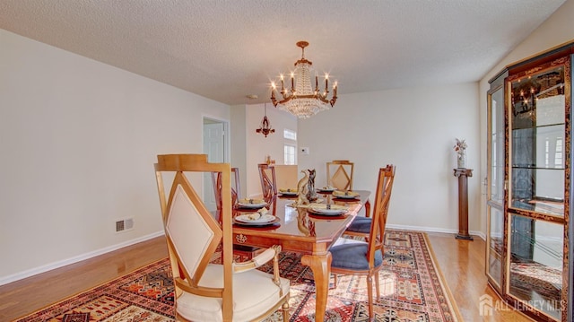 dining area with a textured ceiling, hardwood / wood-style flooring, and a notable chandelier