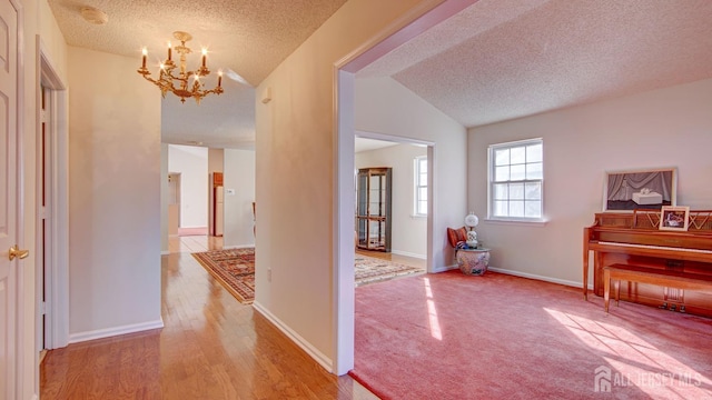 hall featuring a notable chandelier, vaulted ceiling, a textured ceiling, and hardwood / wood-style flooring