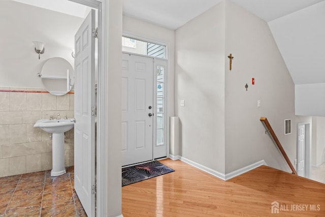 foyer entrance with tile walls, sink, wood-type flooring, and lofted ceiling