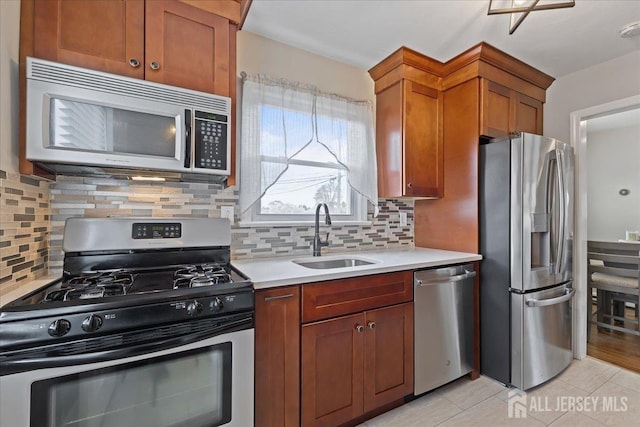 kitchen featuring appliances with stainless steel finishes, a sink, light countertops, light tile patterned flooring, and brown cabinetry