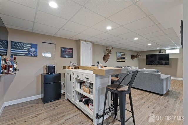 bar with light wood-style flooring, baseboards, freestanding refrigerator, a drop ceiling, and recessed lighting