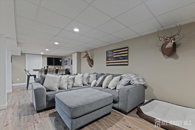 living area with baseboards, a paneled ceiling, light wood-style flooring, bar area, and recessed lighting