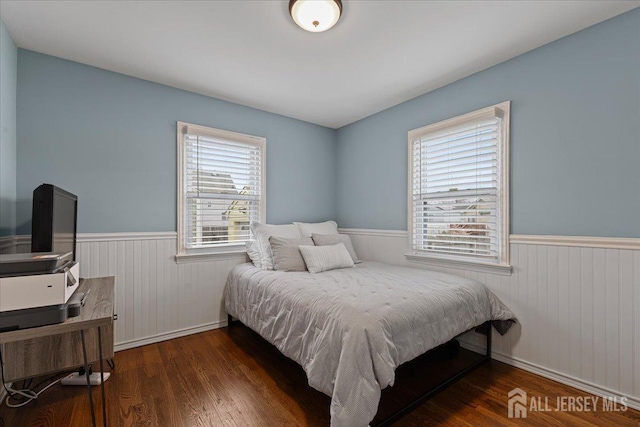 bedroom with a wainscoted wall, wood finished floors, wooden walls, baseboards, and an office area