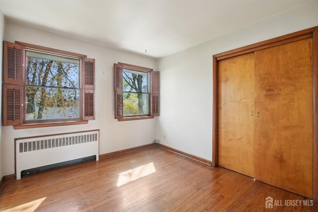 unfurnished bedroom featuring radiator heating unit, wood finished floors, a closet, and baseboards
