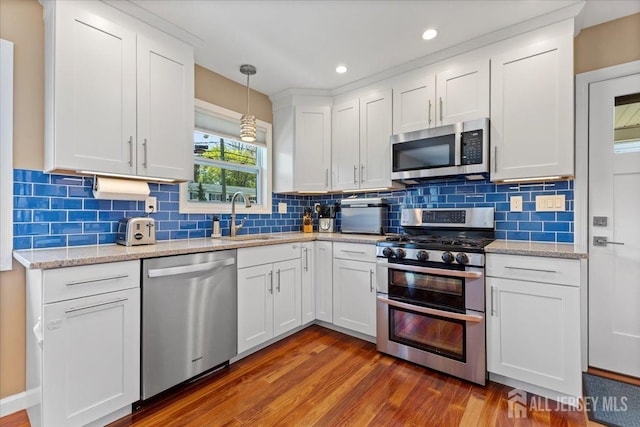 kitchen with appliances with stainless steel finishes, a sink, dark wood finished floors, white cabinets, and backsplash