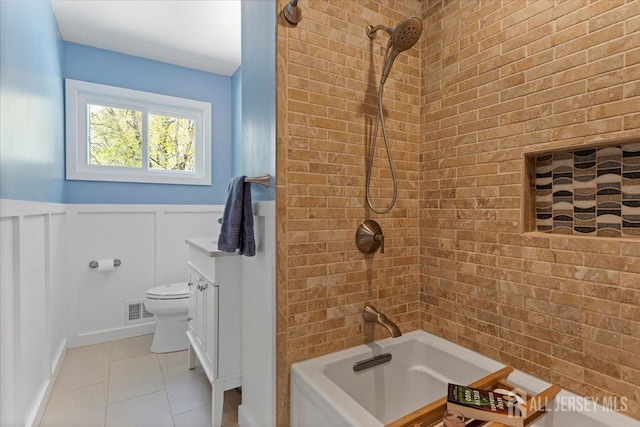 full bathroom with shower / tub combination, toilet, a wainscoted wall, a decorative wall, and tile patterned floors