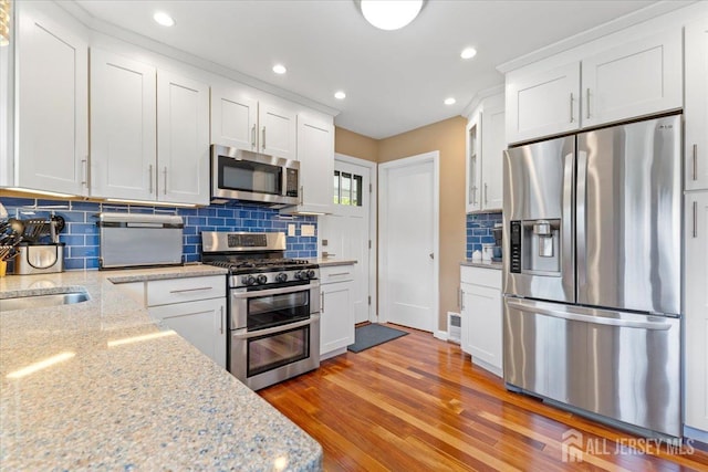 kitchen with stainless steel appliances, backsplash, glass insert cabinets, white cabinets, and light wood-style floors