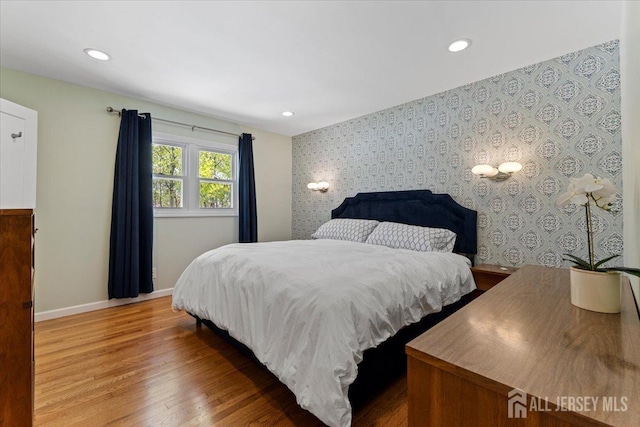 bedroom featuring wood finished floors, baseboards, recessed lighting, wallpapered walls, and an accent wall