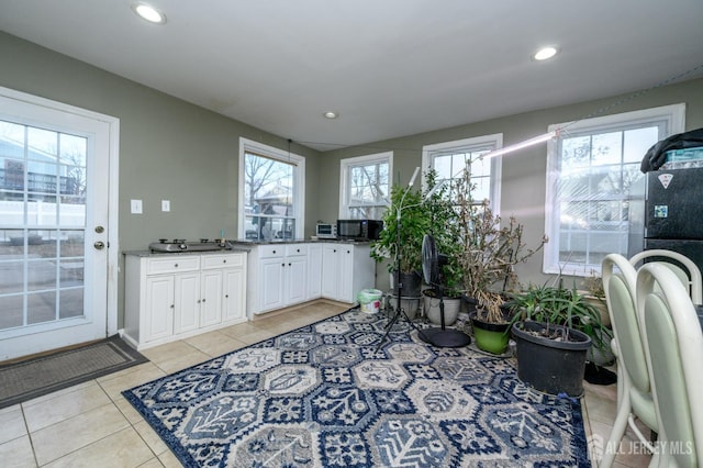 kitchen featuring light tile patterned floors, black microwave, a healthy amount of sunlight, and white cabinetry