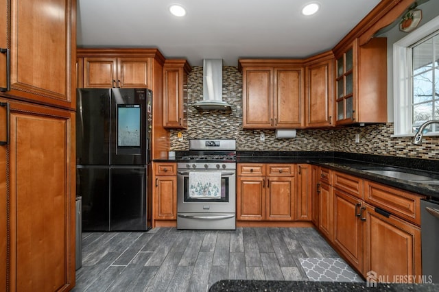 kitchen with stainless steel appliances, wall chimney exhaust hood, a sink, and brown cabinetry