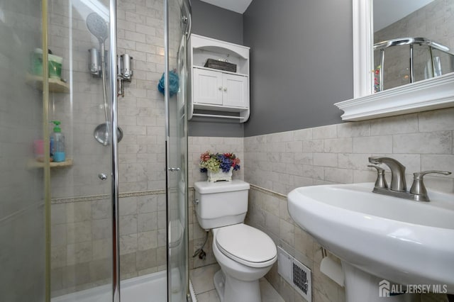 bathroom with toilet, a sink, visible vents, tile walls, and a stall shower