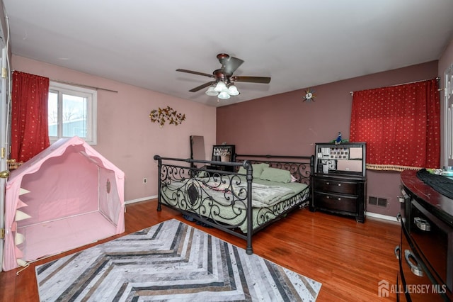 bedroom with a ceiling fan, baseboards, visible vents, and wood finished floors