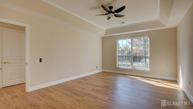 spare room with light wood-type flooring, a tray ceiling, ceiling fan, and ornamental molding