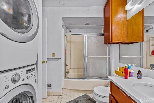 full bathroom with toilet, shower / bath combination with glass door, stacked washer / drying machine, tile patterned flooring, and vanity