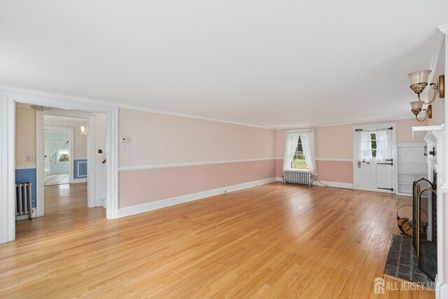 unfurnished living room with light wood-type flooring, radiator heating unit, and crown molding