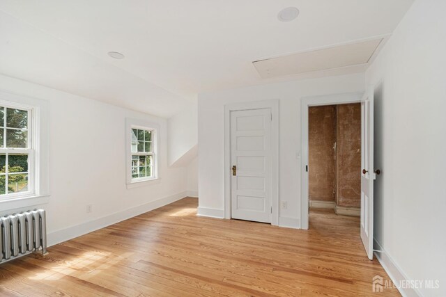 unfurnished room with lofted ceiling, radiator, and light hardwood / wood-style flooring