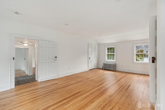 empty room featuring light wood-type flooring, radiator, and lofted ceiling