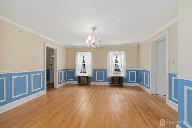 unfurnished room with radiator heating unit, light hardwood / wood-style floors, ornamental molding, and a notable chandelier