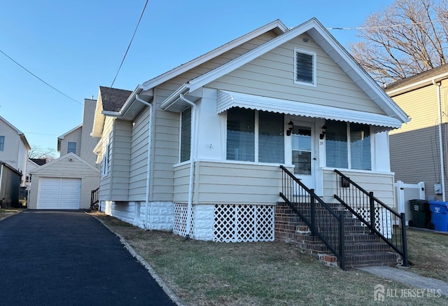 bungalow featuring a garage, covered porch, aphalt driveway, and an outbuilding