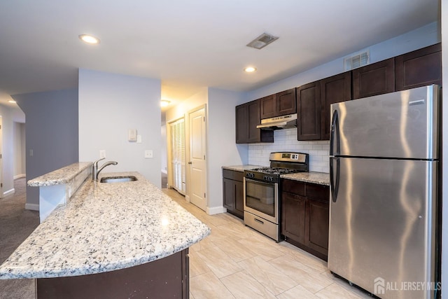 kitchen featuring light stone countertops, decorative backsplash, sink, stainless steel appliances, and a center island with sink