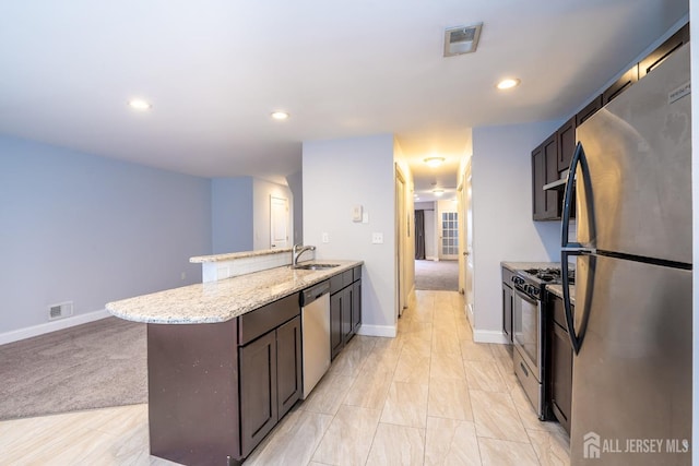 kitchen featuring appliances with stainless steel finishes, sink, light stone counters, a center island, and dark brown cabinetry