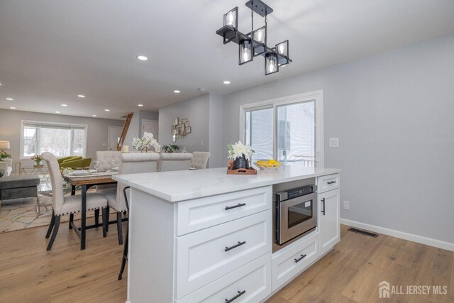 kitchen featuring hanging light fixtures, light wood-type flooring, stainless steel microwave, a kitchen island, and white cabinets