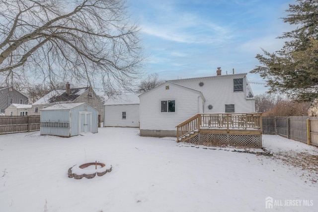 snow covered house with a storage shed, a deck, and an outdoor fire pit