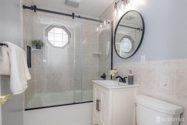 full bathroom with vanity, combined bath / shower with glass door, tile walls, and toilet