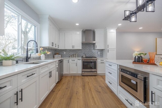 kitchen featuring appliances with stainless steel finishes, sink, white cabinets, backsplash, and wall chimney exhaust hood