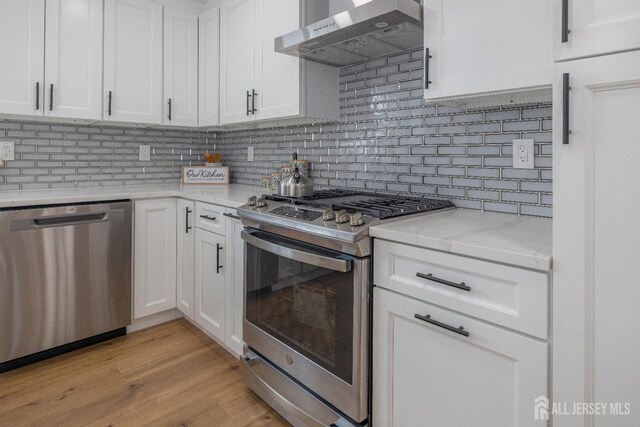 kitchen featuring stainless steel appliances, white cabinetry, wall chimney range hood, and backsplash