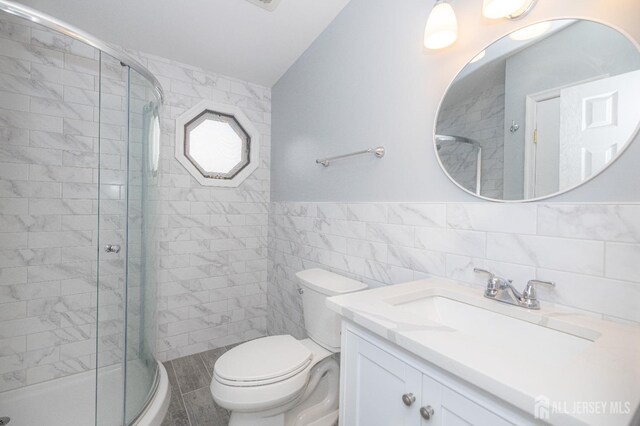 bathroom with tile walls, vanity, toilet, and walk in shower