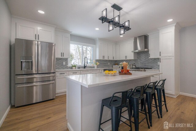 kitchen with wall chimney range hood, light hardwood / wood-style flooring, appliances with stainless steel finishes, white cabinetry, and a center island