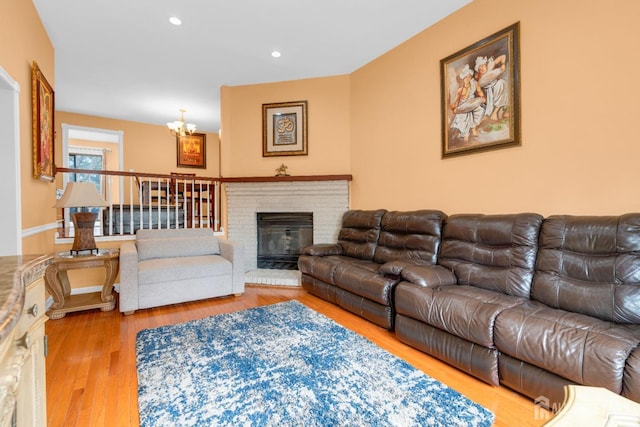 living room with recessed lighting, wood finished floors, a notable chandelier, and a brick fireplace