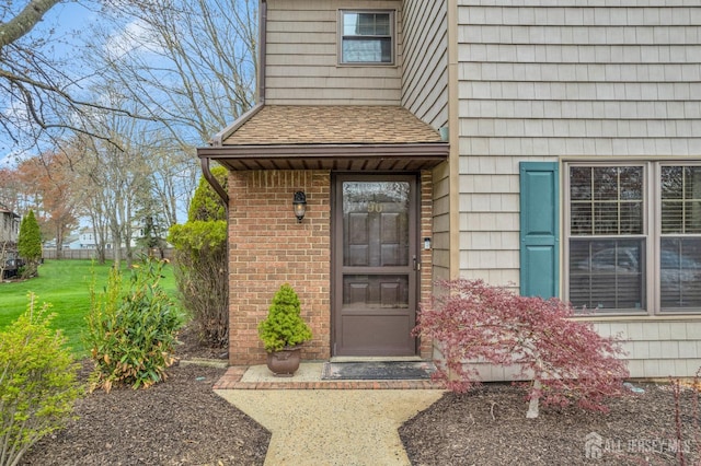 entrance to property with roof with shingles and brick siding